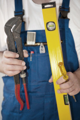 Handwerker im Blaumann hat eine Zange, einen Schraubenzieher und eine Wasserwaage in der Hand.