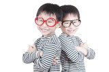 Zwei asiatische Zwillinge in schwarz-weiß gestreiften Oberteilen, bei denen einer eine rote Brille und der andere eine schwarze Brille auf hat.