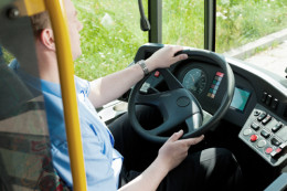 Busfahrer im blauen Hemd sitzt hinter dem Steuer und hat das Lenkrad in der Hand.