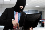 Geschäftsmann mit Sturmmaske und einem offenen Laptop in der Hand steht in einem Büro.