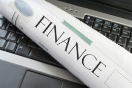 Zeitung "Finance" liegt zusammengerollt auf der Tastatur eines Laptops.