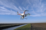 Drohne mit einer Kamera fliegt bei gutem Wetter über ein Feld entlang eines Flusses.