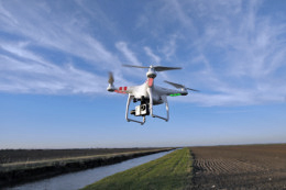 Drohne mit einer Kamera fliegt bei gutem Wetter über ein Feld entlang eines Flusses.