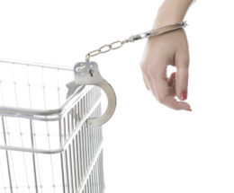 Frau mit roten Fingernägeln an einen Einkaufswagen mit Handschellen gefesselt.