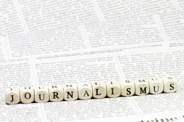 Aneinandergereihte Würfel, die das Wort "Journalismus" ergeben, liegen auf einem Zeitungsartikel.