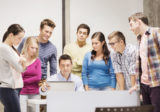 Sieben Schüler stehen im Halbkreis um den Lehrer um schauen sich etwas an.
