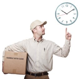 Paketzusteller, der einen Karon mit dem Aufdruck "Handle with care" unterm Arm hält und mit Zeigefinger seiner linken Hand auf ein Uhr zeigt.