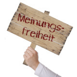 Eine Hand hebt ein Holzschild mit der Aufschrift "Meinungsfreiheit" hoch.