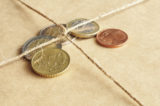 Euromünzen liegen unter einer Paketschnur.