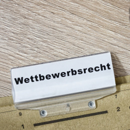 Braune Akte mit der Aufschrift "Wettbewerbsrecht", die auf einem Holztisch liegt. Wettbewerbsrecht