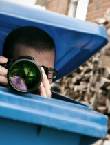 Fotograf mit Kamera, der aus blauer Mülltonne hersausfotografiert.
