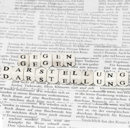 Aneinandergereihte Würfel mit der Aufschrift "Gegen Darstellung" auf einem Zeitungsartikel