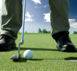 Mann will Golfball in das Loch schießen. Er befindet sich bei schönem Wetter auf dem Golfplatz