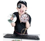 Kind, das sich als Pirat verkleidet hat, hebt zwei CDs in der Hand und steht vor einer Tastatur.
