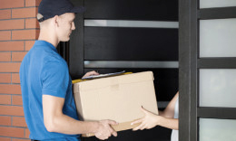 Mann im blauen T-shirt und blauer Kappe übergibt einer Person an deren Haustür ein Paket.