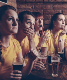 Vier Freunde sitzen in einer Gaststätte, trinken Bier und schauen sich gemeinsam ein Fußballspiel an