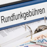 Ordner mit der Beschriftung "Rundfunkgebühren" auf offenem Ordner mit Geldscheinen