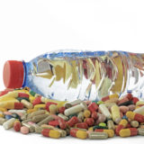 Eine Plastikflasche mit Wasser um die eine Menge Tabletten herumliegen