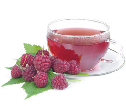 Roter Tee in einem Teeglas mit Himbeeren auf dem Unterteller.