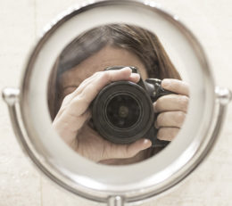 Frau schießt ein Selbstportrait mit einer Kamera durch einen Spiegel