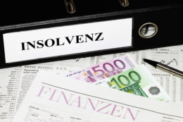 Schwarzer Ordner mit der Aufschrift "Insolvenz" liegt auf Finanzblättern und neben 600 Euro.
