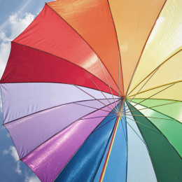 bunter Sonnenschirm in Regenbogenfarben vor blauem Himmel