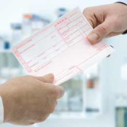 Hand eines Arztes übergibt Arzneimittelrezept an einen Patienten