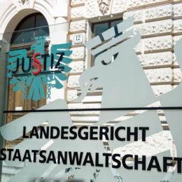 Glasscheibe mit der Aufschrift "Landesgericht Staatsanwaltschaft" vor einem Justizgebäude.