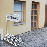 Arztpraxis-Schild mit Fahrradständer vor einem Haus