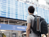 Mann mit Rucksack vor einer Anzeigetafel an einem Flughafen, Reise