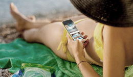 Frau in gelbem Bikini auf grünem Handtuch am Strand mit Smartphone in der Hand