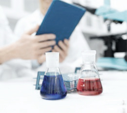 Zwei Personen sind in einem Labor. Vor ihnen steht eine blaue und eine rote Flüssigkeit.