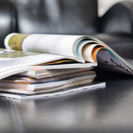 Stapel mit Zeitschriften und Magazinen auf einem Couchtisch, im Hintergrund ein schwarzer Sessel