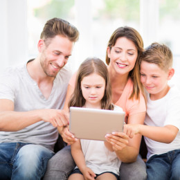 Familie - bestehend aus Vatter, Mutter, Mädchen und junge - sitzt vor einem goldenen Tablet