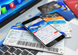 Smartphone mit geöffnetem Flugbuchungsportal liegt auf Laptop mit Flugtickets und Kreditkarten