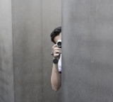 Mann hält Fotoapparat und bleibt hinter einer grauen Wand im Verborgenen