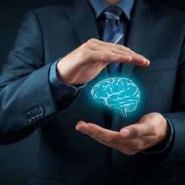 Mann im Anzug hält zwischen seinen Händen ein blaues Gehirnsymbol.