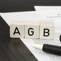 3 Würfel mit den Buchstaben "AGB" auf einem beschriebenen Papier mit einem Stift