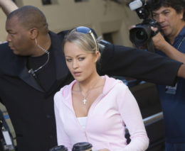 Blonde Frau in Rosa Pullover wird von ihrem Bodyguard vor Paprazzi abgeschirmt