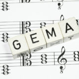weiße Würfel mit der Aufschrift GEMA auf Musiknoten