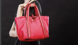 Rote Handtasche wird von einer Frau vor einem schwarzen Hintergrund getragen.