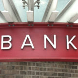 Rotes Schild an einem Gebäude, auf dem in weißer Schrift Bank steht