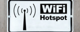 WiFi-Hotspot-Schild in schwarz weiß vor einer Holzwand.