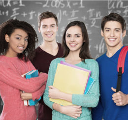 Vier Schüler stehen vor einer Tafel und lächeln.