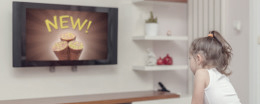 Kleines blondes Mädchen sitzt vor dem Fernseher und schaut Werbung.