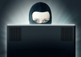 Maskierter Mann sitzt hinter einem Computer-Bildschirm