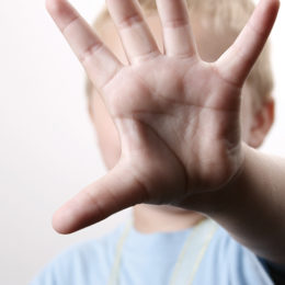 Kind schirmt sich mit seiner Hand ab und nimmt Abwehrhaltung ein