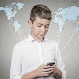 Kind hält Handy in der Hand im Hintergrund eine Weltkarte