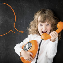 kleines Kind schreit durch ein altes, oranges Drehscheibentelefon, vor dem schwarzen Hintergrund ist ausserdem eine orange Sprechblase zu sehen