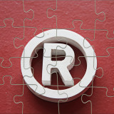 Weißes Trade-Mark-Symbol vor rotem Hintergrund in Puzzle-Optik